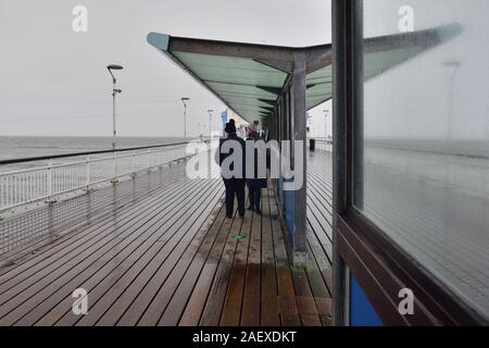 Bournemouth Pier in inverno, Dorset, Regno Unito, dicembre 2019. Il freddo con heavy rain. Due persone riparo dal vento e dalla pioggia. Foto Stock