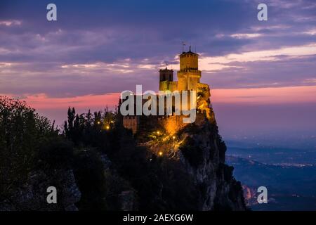 Vista dell'illuminato Guaita Fortezza sul Monte Titano, paesaggio montuoso nella distanza di notte Foto Stock