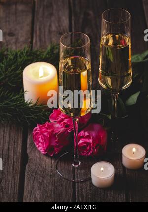 Due bicchieri di champagne con il Rosa Rose e candele accese su una tavola in legno rustico Foto Stock