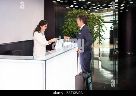 Imprenditore maturo dando business card a receptionist Foto Stock