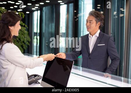 Receptionist dando business card a imprenditore Foto Stock