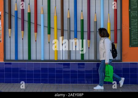 Donna che cammina da store window display di matite colorate, a Ubeda, Provincia di Jaen, Spagna Foto Stock