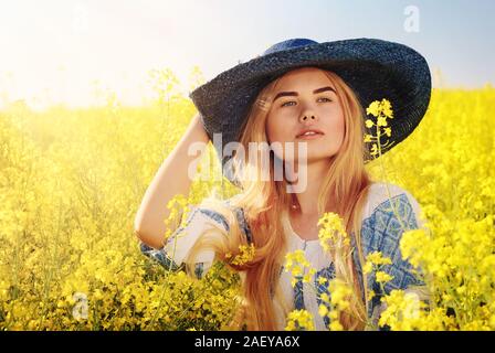 Giovane donna ritratto in rumeno camicetta (IE ABBIGLIAMENTO) sul campo di colza in fiore Foto Stock