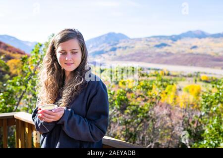 Giovane donna in piedi che guarda lontano nel giardino di casa di bere tenendo tazza da tè con vista delle montagne rocciose in Aspen Colorado durante l'autunno Foto Stock