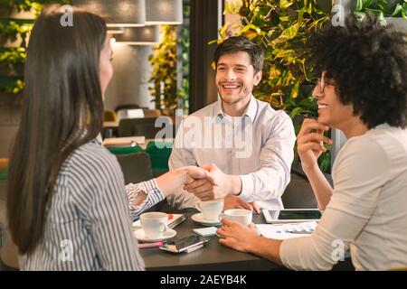 Partnership di successo. Popolo millenario handshaking dopo aver raggiunto un accordo durante il pranzo di lavoro nel cafe, spazio vuoto Foto Stock