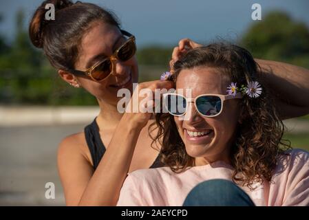 Due donne al di fuori di ridere e di mettere i fiori nei capelli. Foto Stock