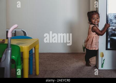 Sorridente multirazziale 2 yr old girl in piedi su un tappeto accanto alla parete Foto Stock