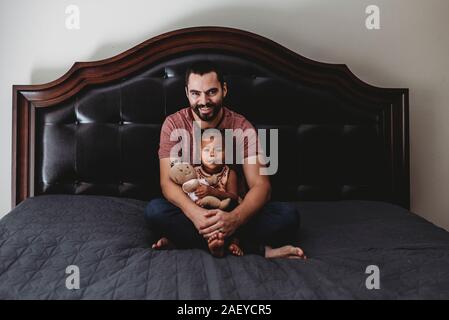 Papà sorridente e 2 anni figlia multirazziale con bambola seduta sul letto Foto Stock