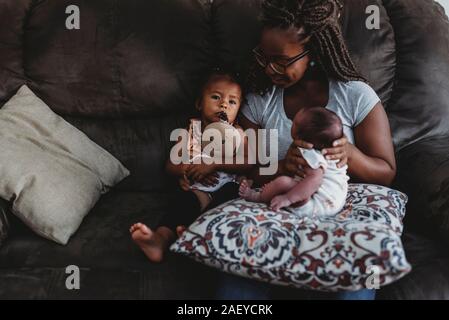 Mom etnico con gli occhiali sul divano con multirazziale e bambino di 2 anni. Foto Stock