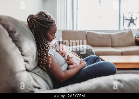 Madre etnica con lunghe trecce sul divano holding multirazziale neonato Foto Stock
