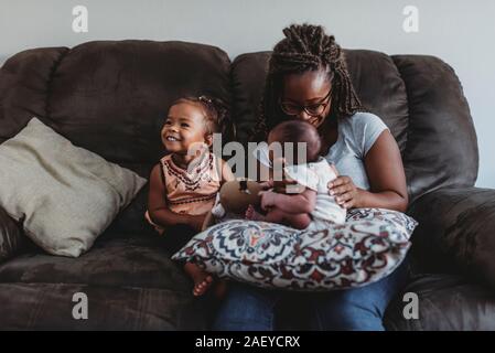 Famiglia multirazziale sul divano come mom neonato tiene accanto alla ragazza sorridente Foto Stock