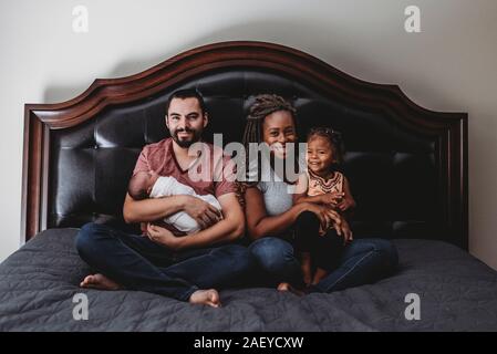 Famiglia multirazziale insieme sul letto - Papà, mamma, infantili e 2 anni. Foto Stock