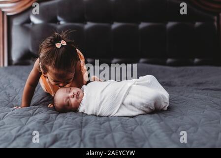 Dolce multirazziale 2 yr old girl sul letto con swaddled gemelli neonati Foto Stock