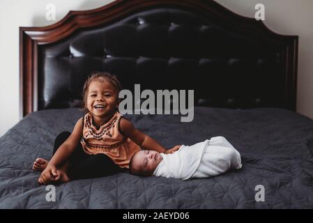 Sorridente biracial 2 yr old girl sul letto con i gemelli neonati Foto Stock