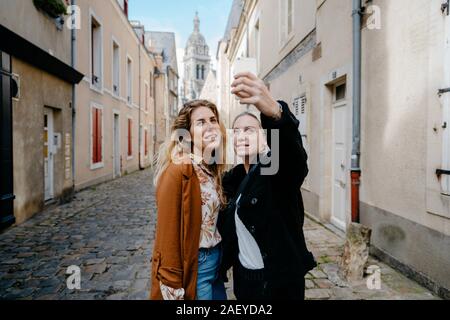 Giovani donne tenendo selfie in una tipica cittadina francese della strada Foto Stock