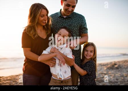 Famiglia di quattro giocando e sorridente sulla spiaggia al tramonto Foto Stock