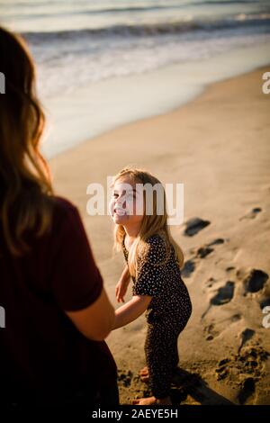 Figlia sorridente al Mom sulla spiaggia al tramonto Foto Stock