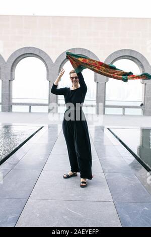 Giovane donna in piedi e tenendo le sue sciarpa colorata sul vento Foto Stock
