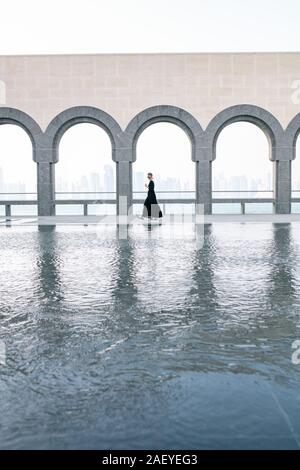 Giovane donna in Lungo abito nero a piedi dal pool nel museo Foto Stock