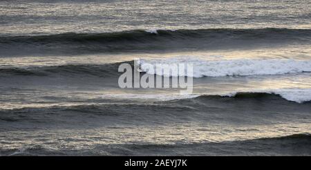 Un surfista effettuare la sua scelta dell'onda e le piastre o decolla su un point break a onda Langland Bay nel Galles del Sud Foto Stock