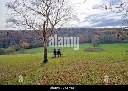 Due donne di mezza età seduto sul sedile cercando di fronte a un paesaggio invernale nel Surrey Hills in comune Ranmore vicino a Dorking England Regno Unito Foto Stock