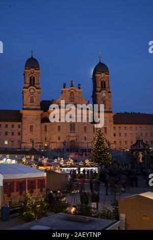 Einsiedler Weihnachtsmarkt (mercatino di Natale) nella parte anteriore del monastero di Einsiedeln all'alba con un albero di natale, cabine e la luna brilla sopra. Foto Stock