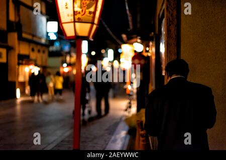 Kyoto, Giappone - Aprile 9, 2019: vicolo buio street di notte nel quartiere di Gion a notte con salaryman permanente illuminata dalla lanterna rossa Foto Stock