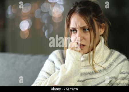 Donna nervoso mordere le unghie in inverno seduto su un divano nella notte a casa Foto Stock