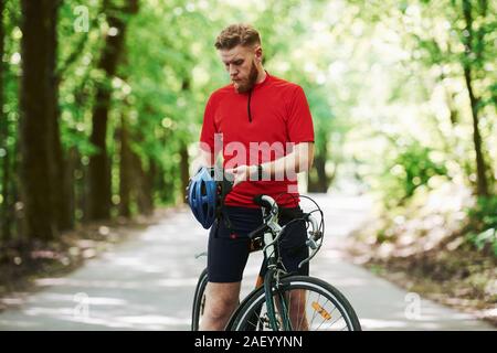 Togliere casco protettivo. Ciclista in sella a una moto è sulla strada asfaltata nel bosco al giorno di sole Foto Stock