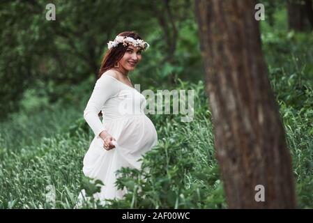 Avente un buon tempo. Bella donna incinta nel vestire una passeggiata all'aperto. Bruna positivo Foto Stock