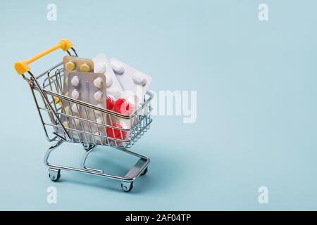 Miniatura carrello della spesa pieno di pillole su sfondo blu. La sanità, l'acquisto di medicinali. Foto Stock