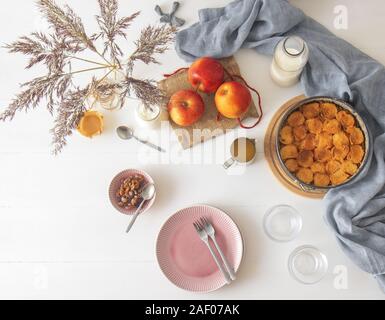 Bianco tavolo in legno con Apple il budino di pane e burro, jar con panna acida, bicchiere di latte, sfondo decorato con alcune mele e vaso a secco con gra Foto Stock