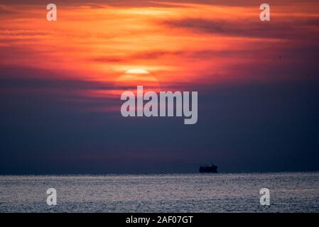 La scena del tramonto sul mare. Rosso drammatico il cielo sopra la silhouette di una nave in calme acque del mare. Foto Stock