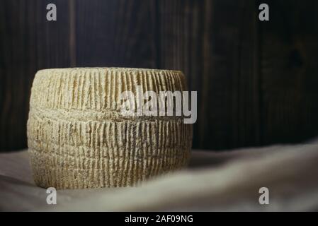 Maasdam testa di formaggio su uno sfondo scuro di tavole di legno e carta pergamena. Disco di formaggio di capra su uno sfondo scuro. Il concetto di azienda artigianale formaggio di latte di vacca. Foto Stock