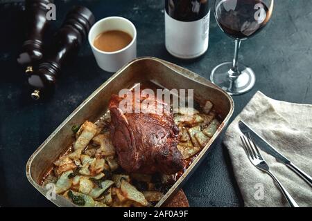 Un grande pezzo di carne cotta al forno con patate su un vassoio con salse Foto Stock
