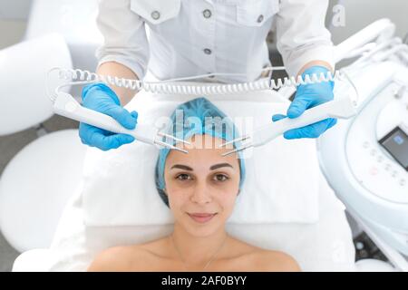 Ritratto di una giovane ragazza bella faccia terapia microcurrent procedura. Cura del viso e il ringiovanimento. Aumento del tono epidermico. Foto Stock