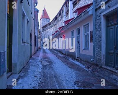 Stretto vicoletto nel centro medievale della città vecchia di Tallinn al crepuscolo con una torre della cinta muraria in background Foto Stock