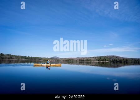 L'uomo paddling una canoa sotto il cielo limpido su di un lago calmo Foto Stock