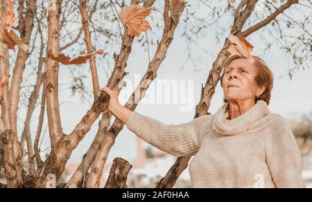 In autunno le foglie che cadono sulla donna senior sul cielo blu Foto Stock