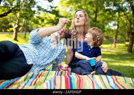 Famiglia soffiare bolle con figlio nel parco Foto Stock