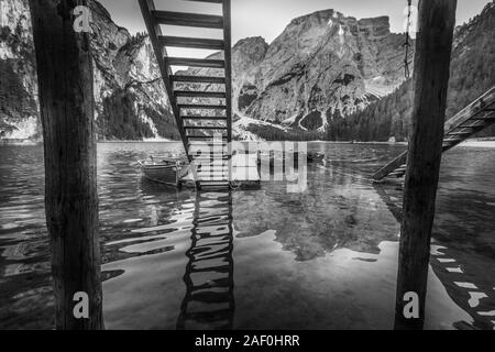 Barche a remi ormeggiate sotto una scala di legno nel lago di Braies effetto bianco e nero Foto Stock