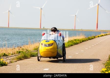 Colorato turbine eoliche in polder, terra recuperata nei pressi di Almere, Flevoland, Paesi Bassi, con un ciclista in un aero dinamica veicolo recumbant. Foto Stock