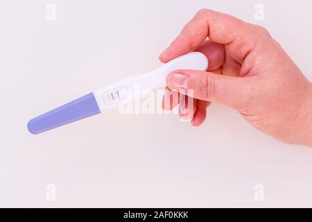 Test di gravidanza in mano femminile che mostra un risultato positivo isolare su sfondo bianco. Foto Stock