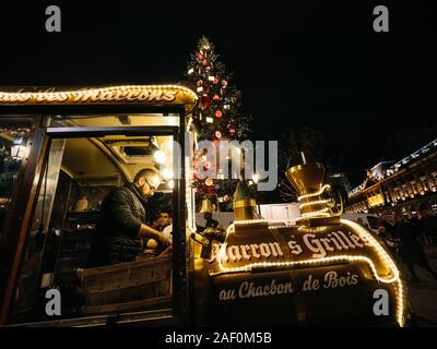 Strasburgo, Francia - Dic 24, 2018: basso angolo di uomo adulto vendita di castagne arrostite dal tradizionale carrozza del treno in Place Kleber per i turisti e i locali durante l'annuale Mercato di Natale Foto Stock