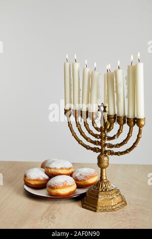 Deliziose le ciambelle nei pressi di candele accese in menorah su Hanukkah isolato su bianco Foto Stock