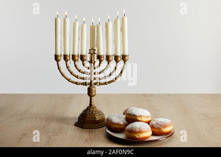 Deliziose le ciambelle nei pressi di candele accese in menorah su Hanukkah isolato su bianco Foto Stock