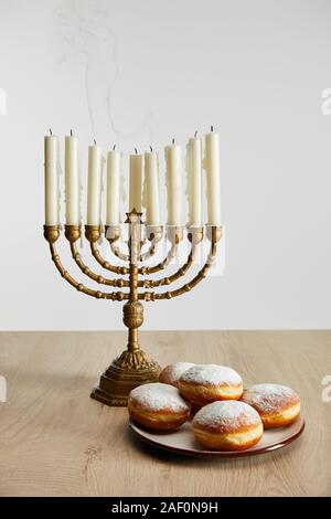 Deliziose le ciambelle nei pressi di candele accese in menorah su Hanukkah isolato su bianco Foto Stock