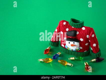 maglione rosso con collo verde e maniche bianche fiocchi di neve e pupazzo di neve con cappello nero e naso di carota isolato su uno sfondo rosso festoso Foto Stock