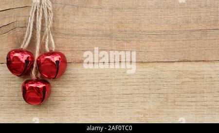 Tre rossi Jingle Bells appeso alla fune contro uno sfondo di legno con spazio di scrittura Foto Stock