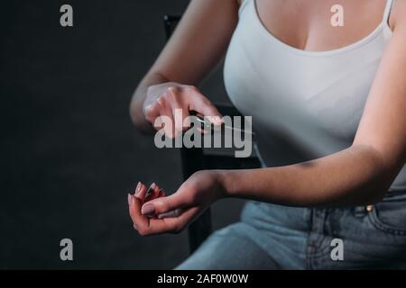 Vista ritagliata della donna di suicidarsi dal taglio di vene con rasoio su sfondo scuro Foto Stock